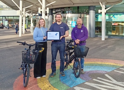 Three individuals posing outside a hospital with a certificate